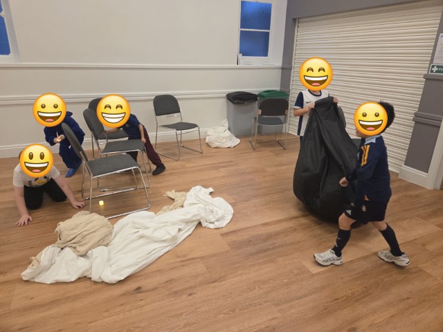 Boys preparing to make a tent in the hall - with emojis covering their faces for privacy