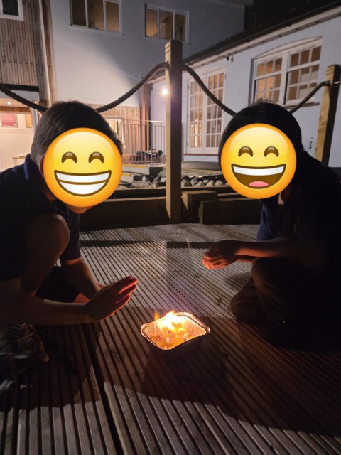 Boys warming their hands over a small fire - with emojis covering their faces for privacy