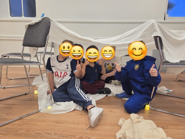 Boys giving a big thumbs up in the tent they've made - with emojis covering their faces for privacy
