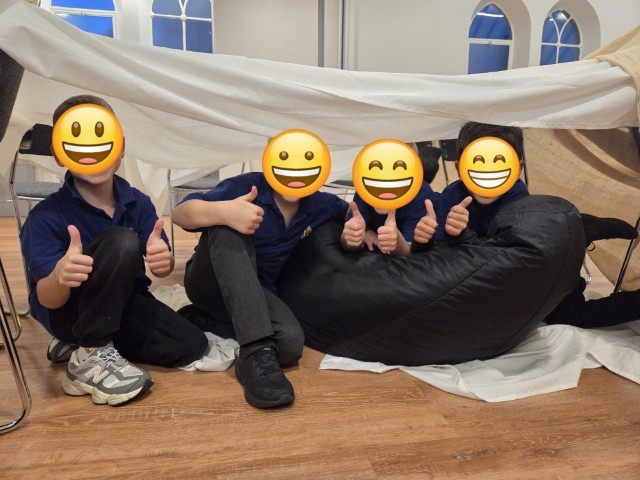 Boys giving a big thumbs up in the tent they've made - with emojis covering their faces for privacy