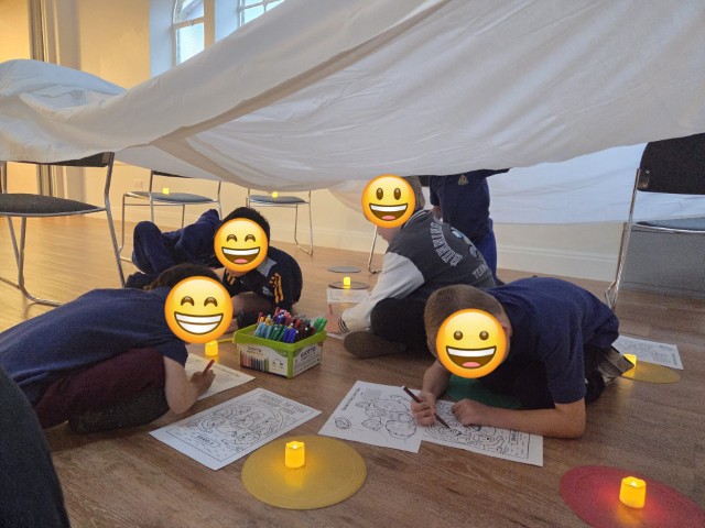 Boys completing activity sheets in the tent they've made - with emojis covering their faces for privacy